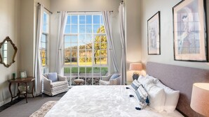 A bedroom with a large bed, two chairs, a small table, and a window with curtains. - Lake David Luxe Lakehouse Getaway (Kangaroo Valley)