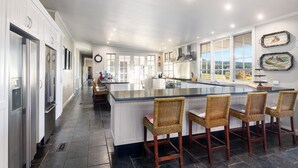 A spacious kitchen with a large island, bar stools, and a view of the outdoors. - Lake David Luxe Lakehouse Getaway (Kangaroo Valley)