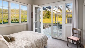 A bedroom with a large bed, a chair, and a sliding glass door leading to a patio with a view of a green landscape. - Lake David Luxe Lakehouse Getaway (Kangaroo Valley)