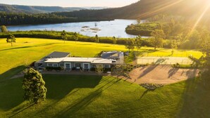 A large house with a tennis court, surrounded by a lush green landscape and a lake. - Lake David Luxe Lakehouse Getaway (Kangaroo Valley)