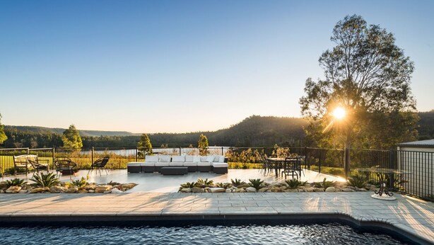 A poolside area with a seating arrangement, a view of the water, and a forested landscape in the background. - Lake David Luxe Lakehouse Getaway (Kangaroo Valley)