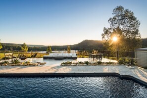 A poolside area with a seating arrangement, a view of the water, and a forested landscape in the background. - Lake David Luxe Lakehouse Getaway (Kangaroo Valley)