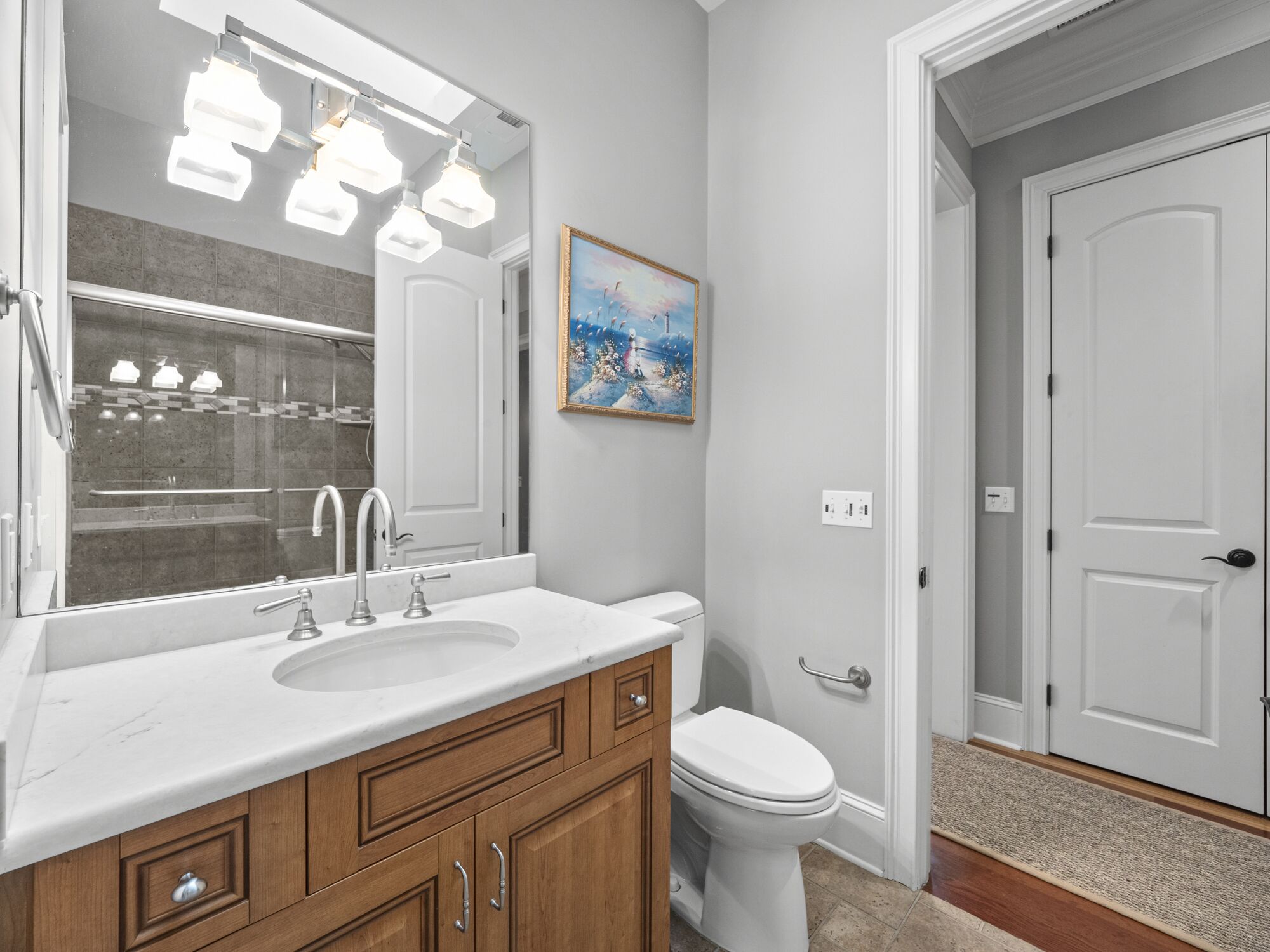 A bathroom with a large mirror, a sink, a toilet, and a door.