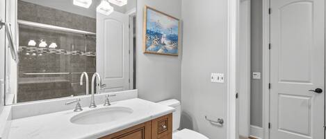 A bathroom with a large mirror, a sink, a toilet, and a door.