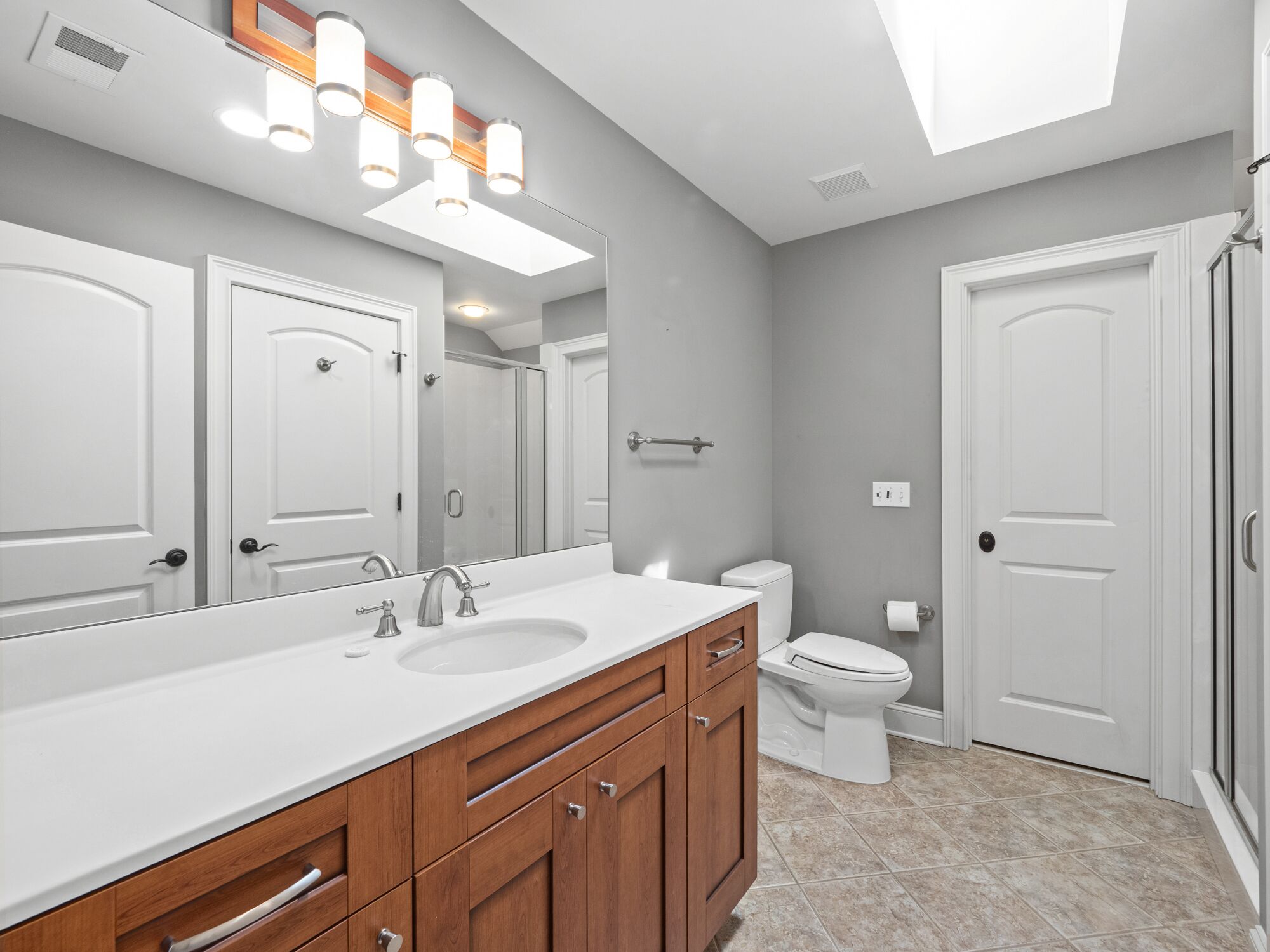 A modern bathroom with a large mirror, two sinks, wooden cabinets, and a toilet.