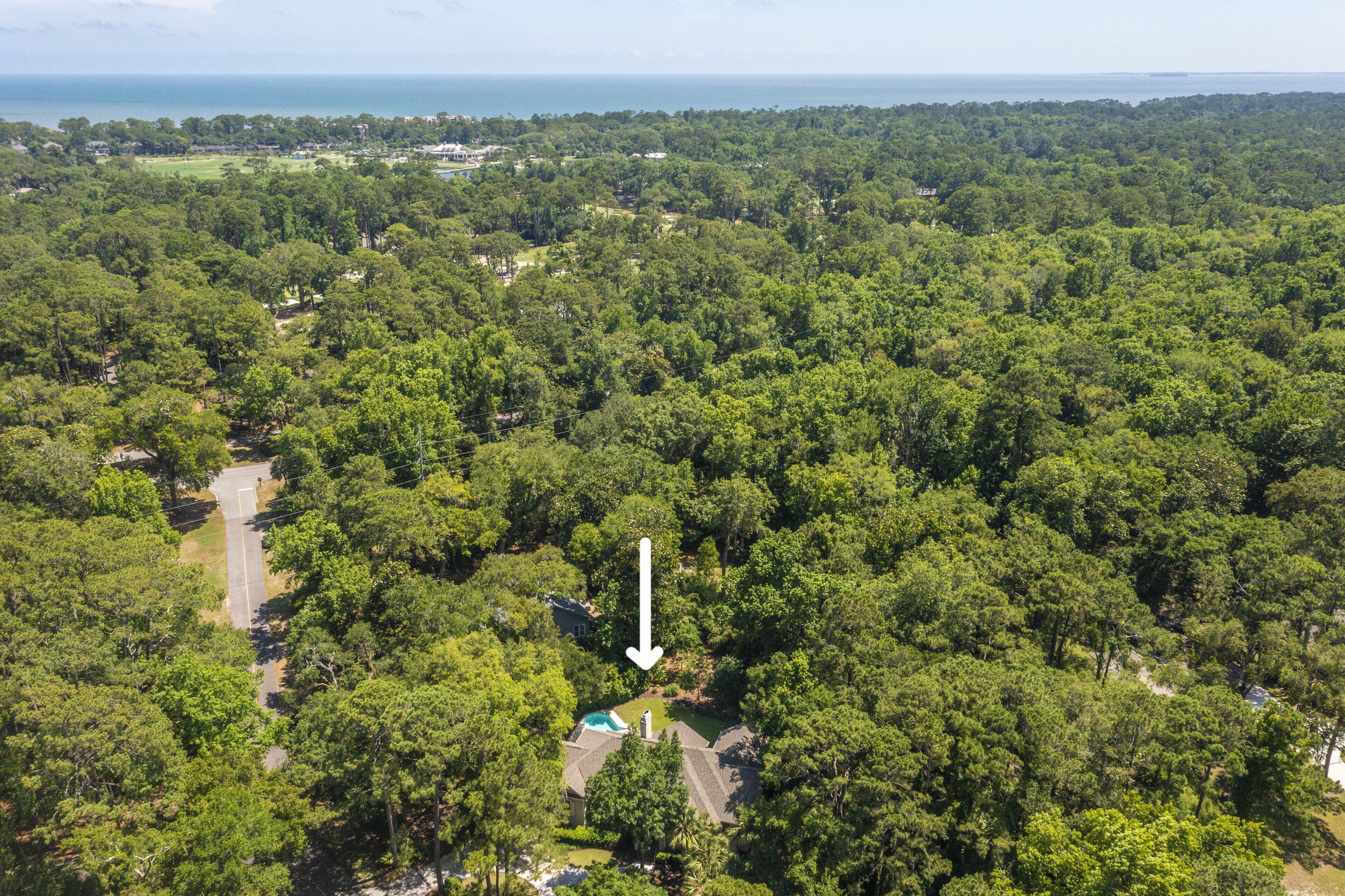 An aerial view of a forested area with a road leading to a house with a swimming pool.
