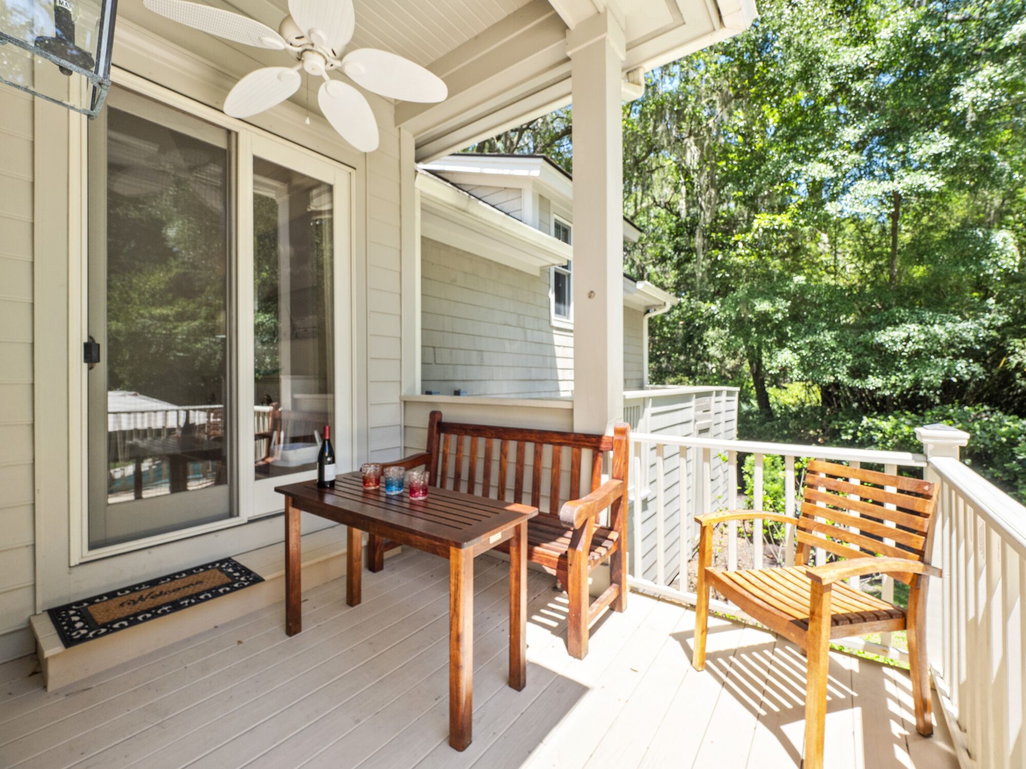 A covered porch with a table and chairs, a ceiling fan, and a view of a house and trees.