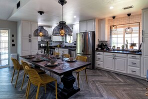 A modern kitchen with white cabinets, a large island, yellow chairs, and pendant lighting.