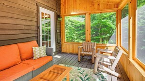 Eine Holzterrasse mit einer Couch und Stühlen, großen Fenstern und einer Tür.