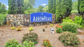 A sign for Lake Arrowhead with a stone wall and landscaped garden.