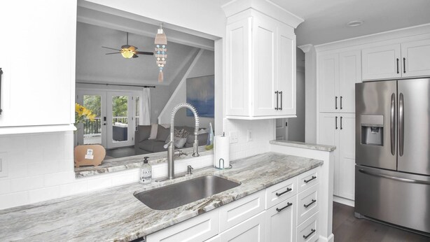 A modern kitchen with white cabinets, a stainless steel refrigerator, and a marble countertop.