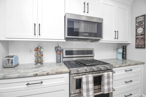 A kitchen with white cabinets, a stainless steel microwave, a gas stove, and a coffee maker. - 2BR+Loft |Screened Patio| Lake Views at Arrowhead |Pool, Tennis, Boating, Hiking, Dining, Pickleball (Waleska)