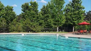 A swimming pool with clear blue water, surrounded by trees and a red umbrella.