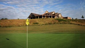 A golf course with a flagstick in the foreground and a large building in the background.