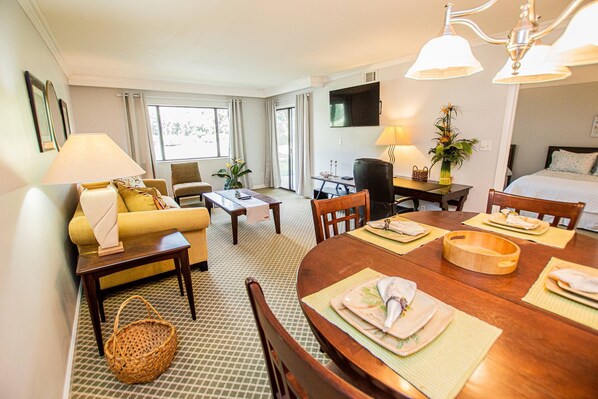 A hotel room with a dining area, a sofa, a TV, and a bed.