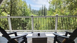 A wooden deck with two lounge chairs and a small table, overlooking a forested area.