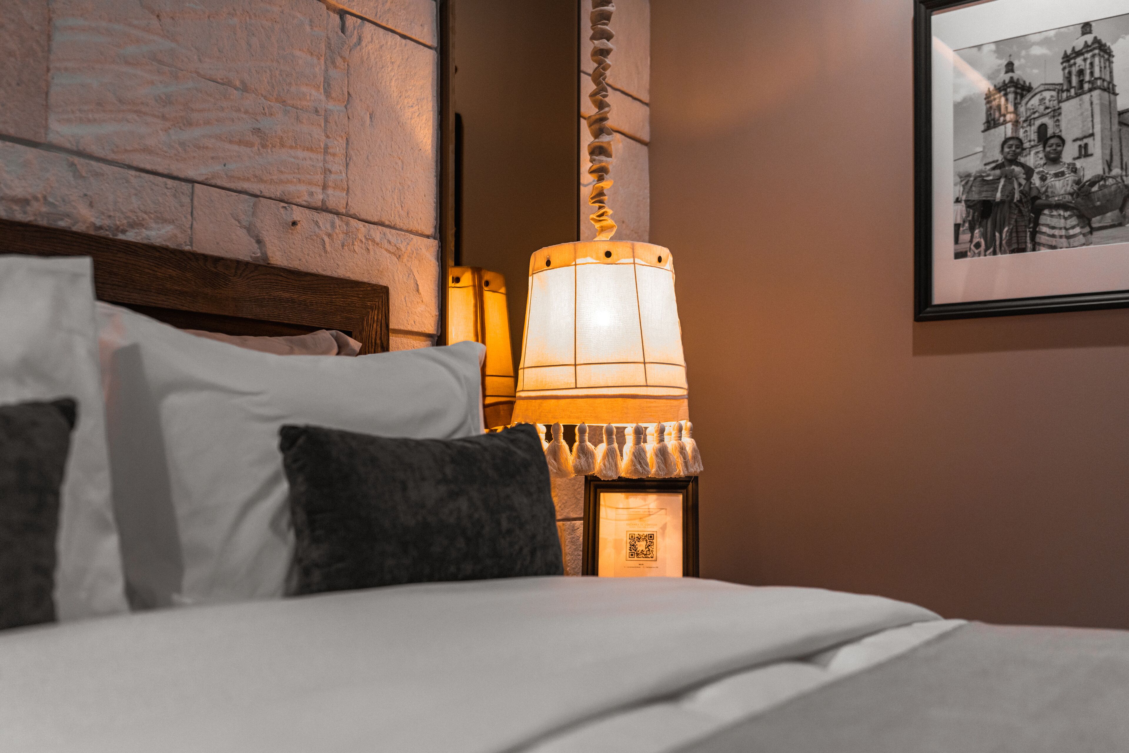 A neatly made bed with white and dark pillows, a wall-mounted picture frame, and a decorative wall piece.
