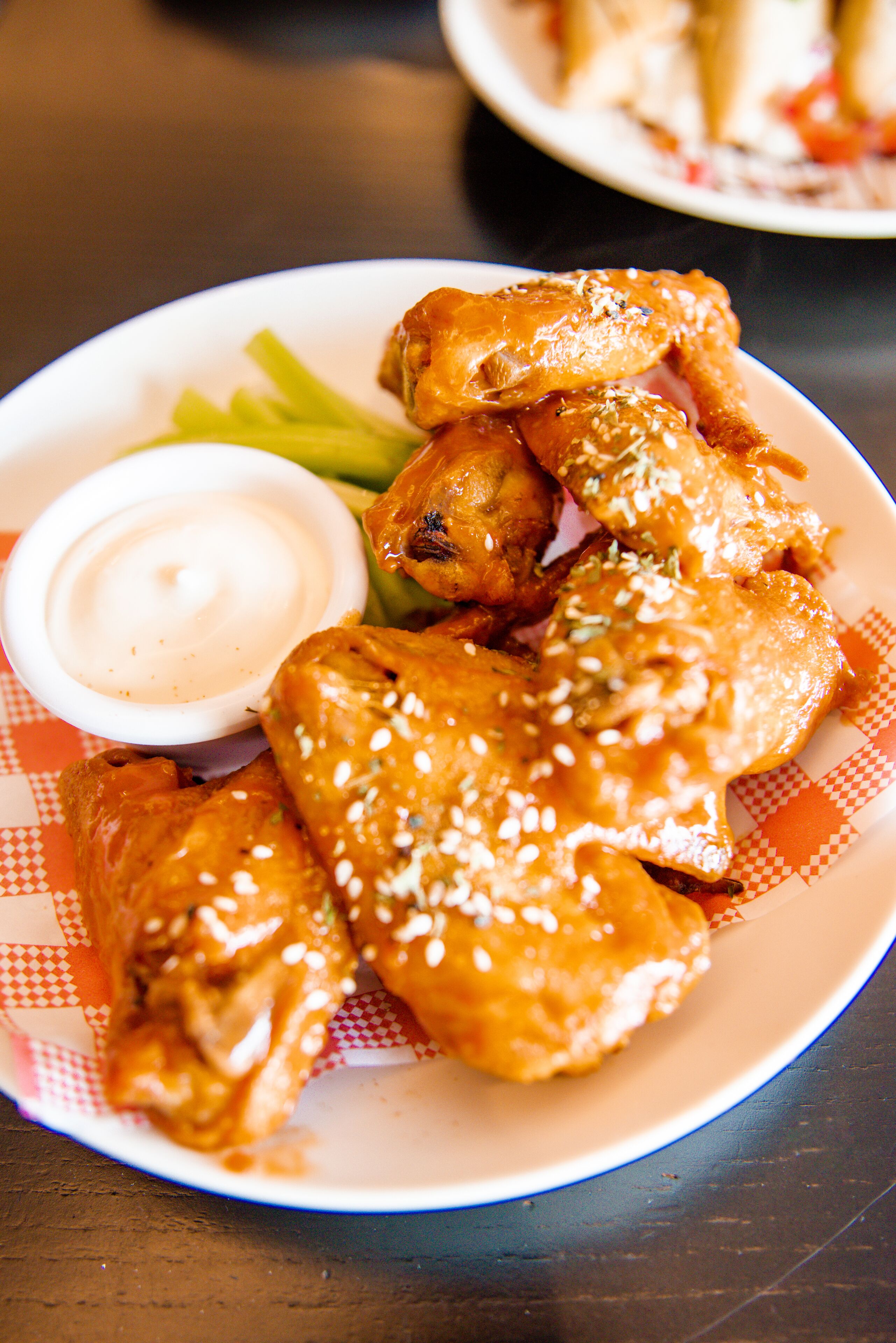 A plate of chicken wings with a dipping sauce and celery sticks.