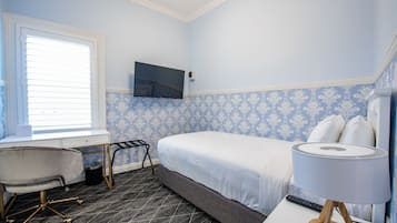 Ett hotellrum med en säng, ett skrivbord med en stol, en tv som är monterad på väggen och en lampa på ett nattduksbord.