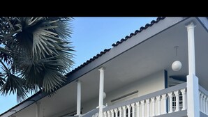 Ein zweistöckiges Gebäude mit weißer Fassade, einer geschwungenen Treppe mit weißen Geländern und einem Balkon mit weißen Säulen.