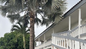 Ein zweistöckiges Gebäude mit weißer Fassade, einem überdachten Balkon und einem gepflegten Rasen.
