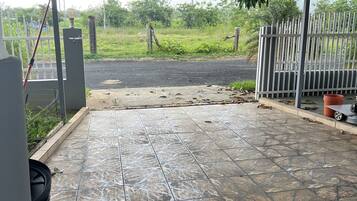 A covered outdoor area with a tiled floor, a metal gate, and a view of a road and greenery.