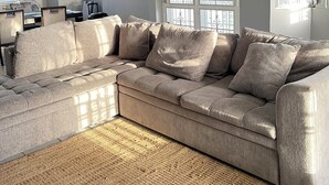 Ein Wohnzimmer mit einem Ecksofa, einem Deckenventilator und großen Fenstern.