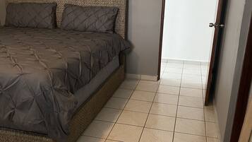 A bedroom with a bed, a door, and tiled flooring.