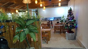 An indoor dining area with wooden tables and chairs, a Christmas tree, and potted plants. - Bunk Bed Room Nusa Penida - Hostel (Penida Island)