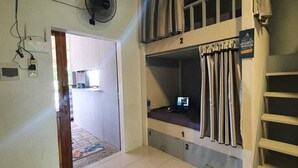A dormitory room with bunk beds, a fan, a television, and a window with curtains. - Bunk Bed Room Nusa Penida - Hostel (Penida Island)