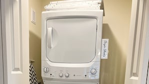 Une petite buanderie équipée d’un lave-linge et d’un sèche-linge superposés, d’une bouche d’aération et d’une serviette à motifs en chevrons.