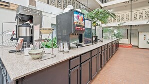 A commercial kitchen with espresso machines, a coffee press, and a large coffee dispenser. - Coratel Suites Deluxe 1 King Suite with Sofa Oversized Non Smoking (Wichita)