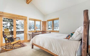 Relax in this serene bedroom with a large bed, high ceiling, and expansive windows offering a view of the outdoors.
