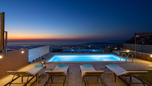 Un espace piscine aménagé sur le toit, avec des chaises longues et une vue sur la ville au crépuscule.