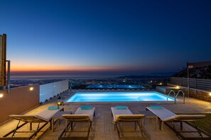 A rooftop pool area with lounge chairs and a view of the city at dusk.