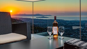 Une table avec une bouteille de vin et deux verres, placée devant un paysage urbain illuminé par les couleurs d’un coucher de soleil.