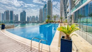 A rooftop swimming pool with a city skyline view, surrounded by modern buildings and palm trees. - Maison Privee - Aesthetic Apt w/ Stunning Vw in Luxurious Building (Dubai)