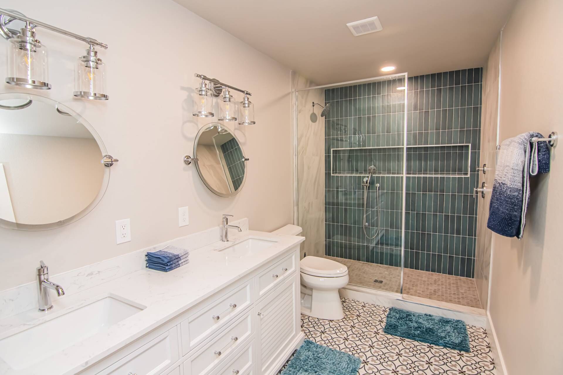 Une salle de bain avec un meuble-lavabo blanc, un miroir rond, une cabine de douche en verre et un carrelage décoratif.