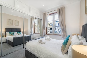 A hotel room with a large bed, a bedside table, a mirror, and a window with curtains. - The Summit West end Spacious City flat with Private parking (Aberdeen)