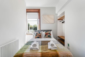 Une chambre à coucher bien rangée, avec un lit, des oreillers, une fenêtre et un radiateur.