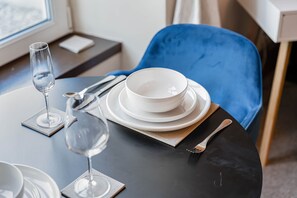 A dining table with plates, a wine glass, and cutlery, set against a blue chair and a window with a view. - The Summit Apartment Westend - Quiet and Cozy West end flat (Aberdeen)