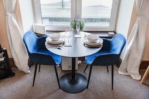 Une table à manger avec deux chaises bleues, des assiettes blanches, un verre et une petite plante.