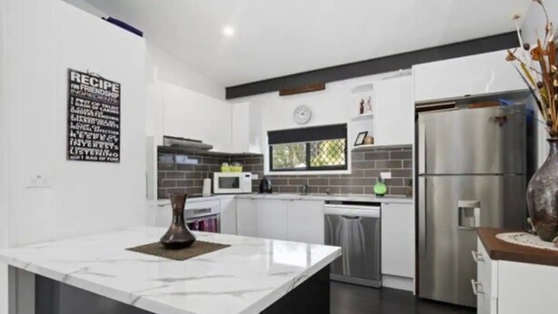A modern kitchen with white cabinetry, a marble countertop, a stainless steel refrigerator, and a decorative vase. - Modern 2 bedroom Unit in the beautiful Scenic Rim (Rathdowney)