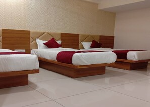 A hotel room with three wooden beds, each with white bedding and red pillows. - Hotel Lux Inn (Ahmedabad)