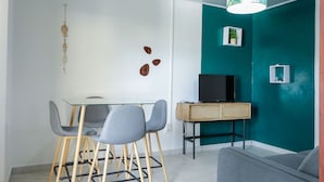 Ein modernes Wohnzimmer mit einer Türkis-farbenen Akzentwand, einem Glastisch mit Stühlen, einer Holzkommode und einem Fernseher.