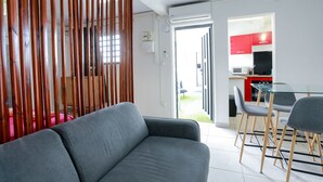 Ein modernes Wohnzimmer mit grauem Sofa, einer Holzabtrennung und einer Küche mit roten Schränken und einem Glastisch.