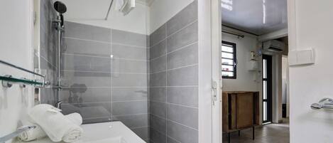 Un baño moderno con bañera, ducha y baldosas grises. Hay un armario de madera y una repisa de vidrio.