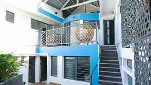 Ein mehrstöckiges Gebäude mit einer Holzterrasse, einer Treppe und einem Balkon mit einem dekorativen Korbstuhl.