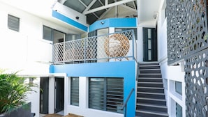 A multi-level building with a wooden deck, a staircase, and a balcony with a decorative wicker chair. - Appart Quattro (Saint Paul)