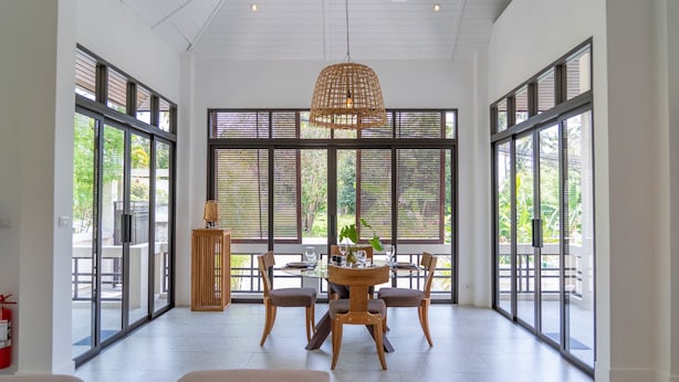 A spacious room with large windows, a dining table with chairs, and a hanging light fixture.